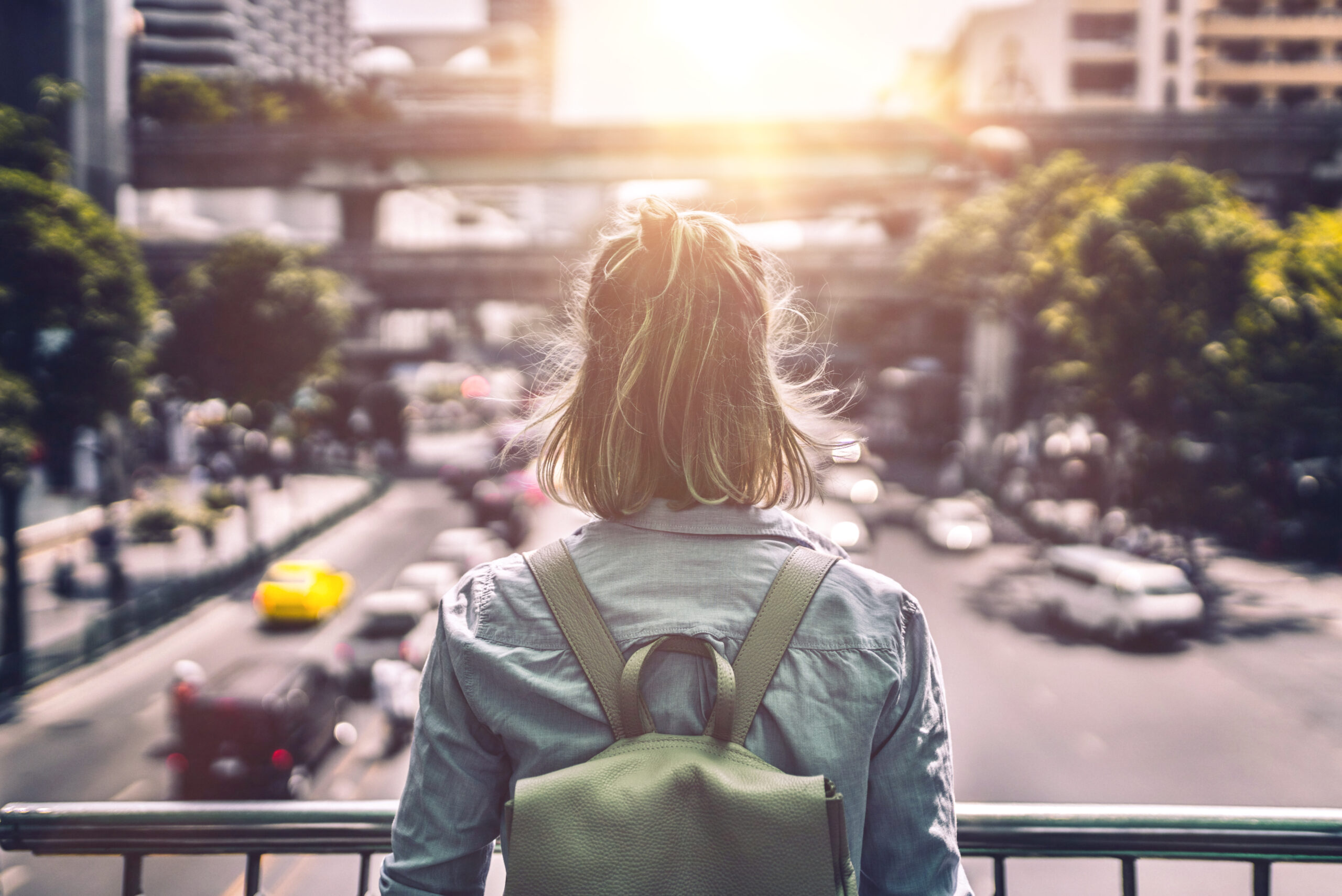 A woman with a backpack is looking out on a blurry city