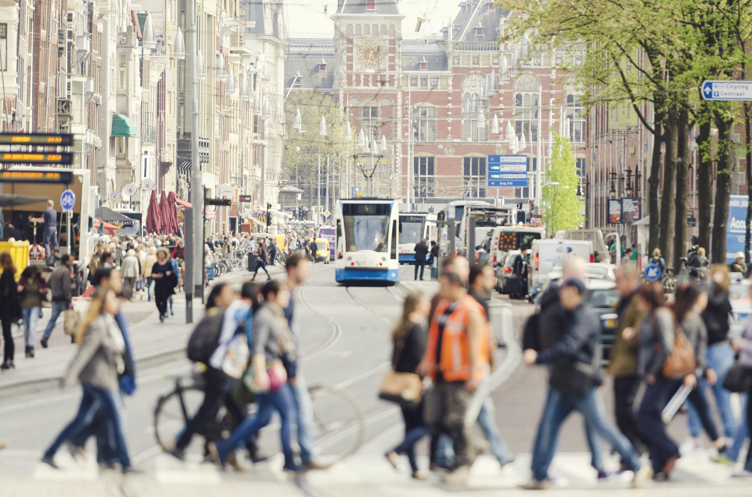 A busy European city with blurry people crossing the street, trams and cars