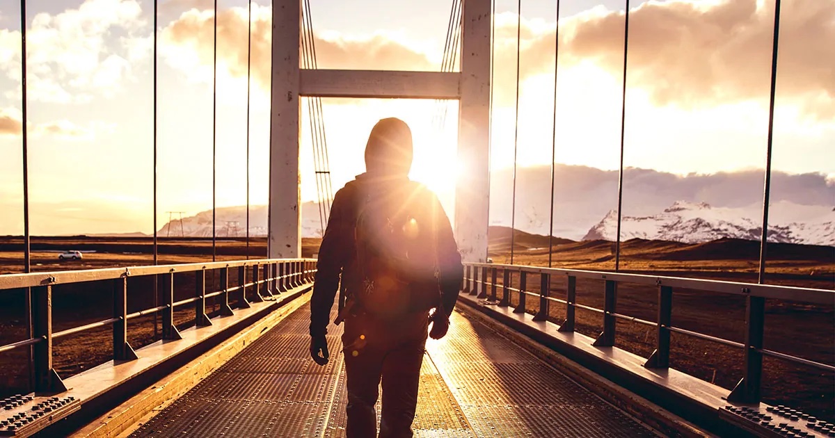 Man with a backpack walking in the sunshine over a bridge