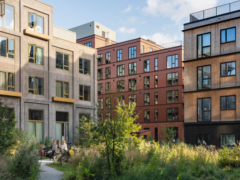Modern apartment buildings with large windows surrounded by greenery and a path for walking.