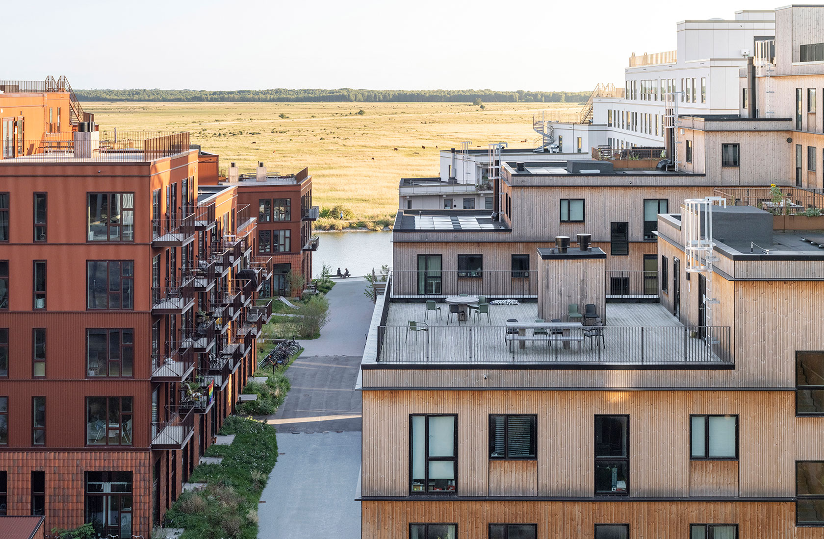 Modern apartment buildings near a canal with farmland in the background under a clear sky.