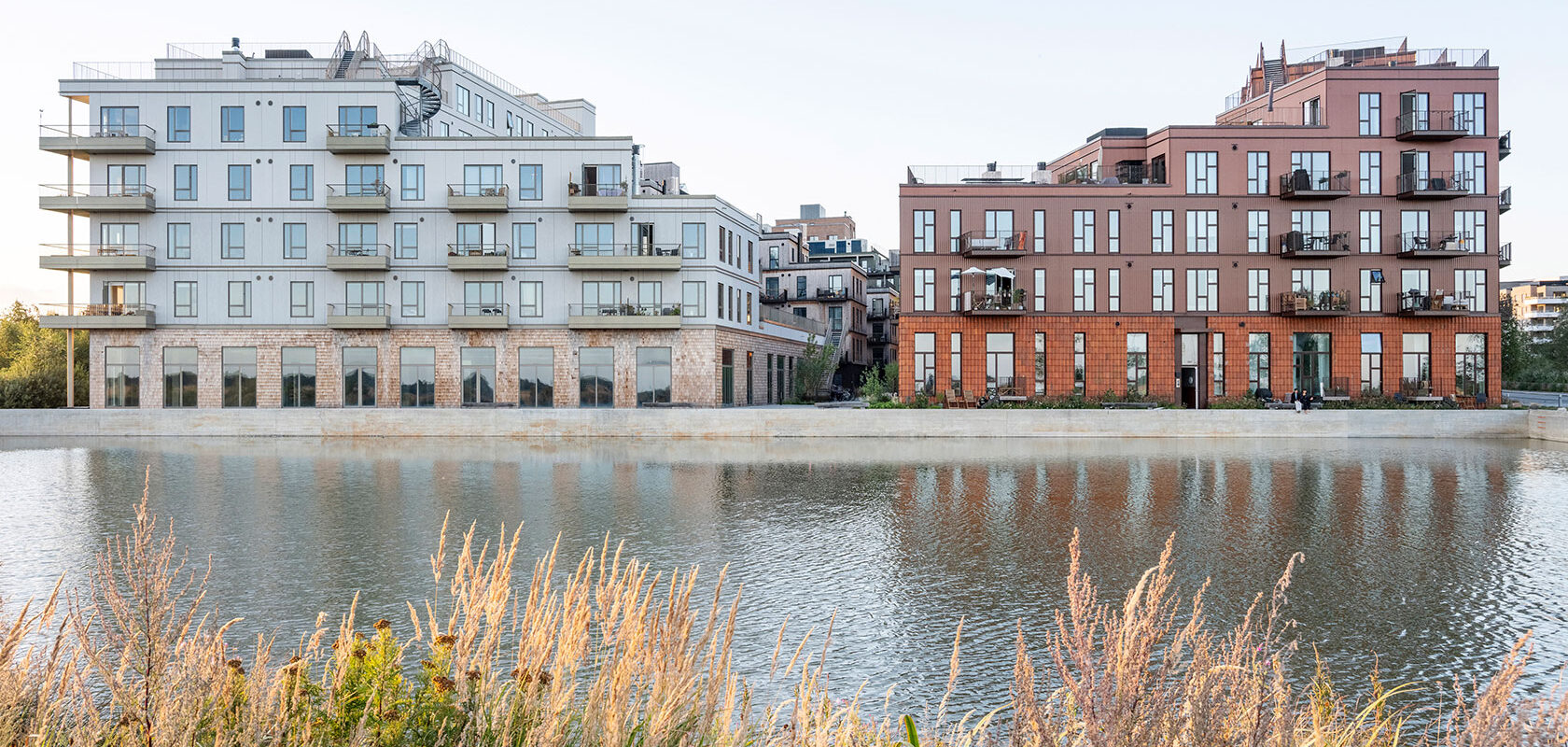 Modern apartment buildings beside water with greenery in the foreground.