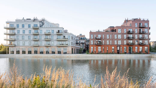 Modern apartment buildings beside water with greenery in the foreground.