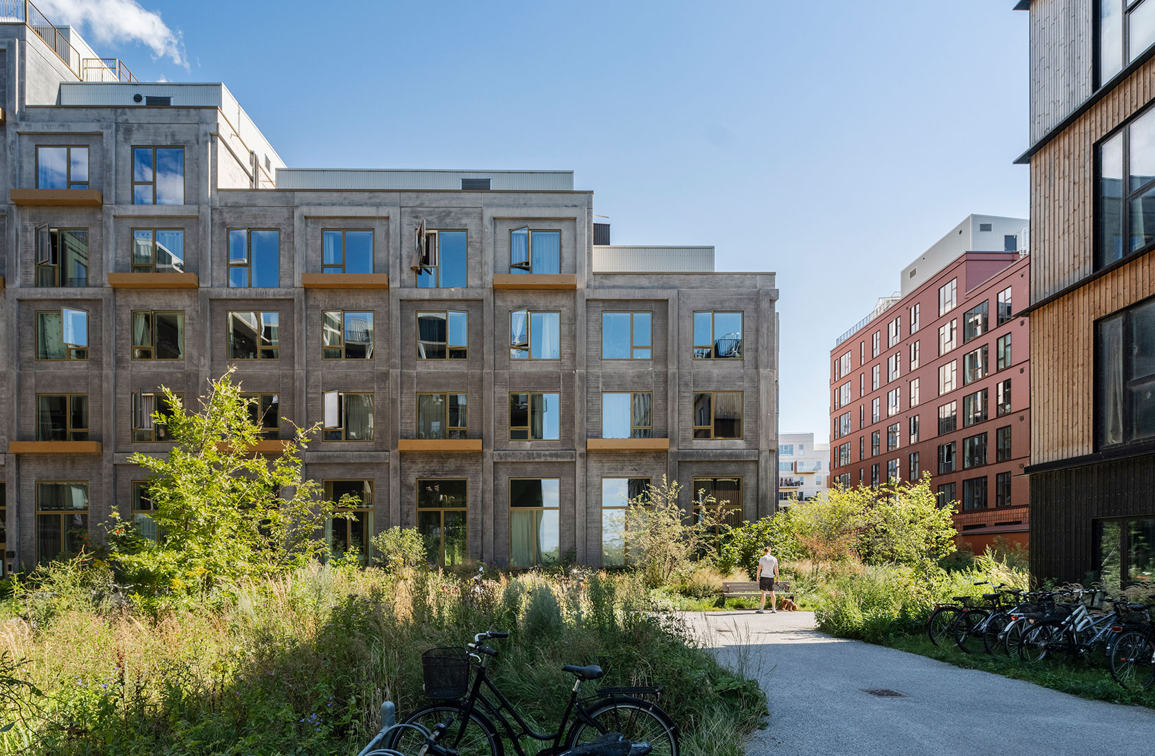 Modern apartment buildings with large windows and a green courtyard on a sunny day.