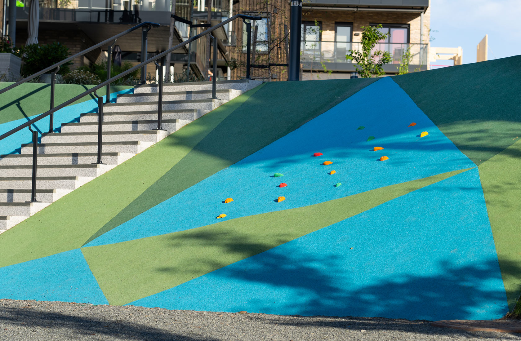 Climbing wall for kids in blue and green with stairs in the background.