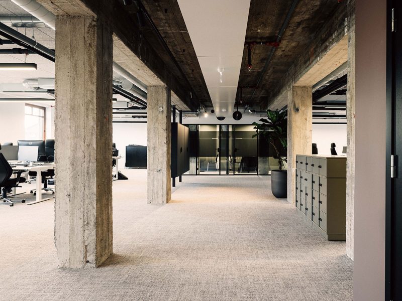 Office space with pillars of concrete a conference room in the background and working places to the left.