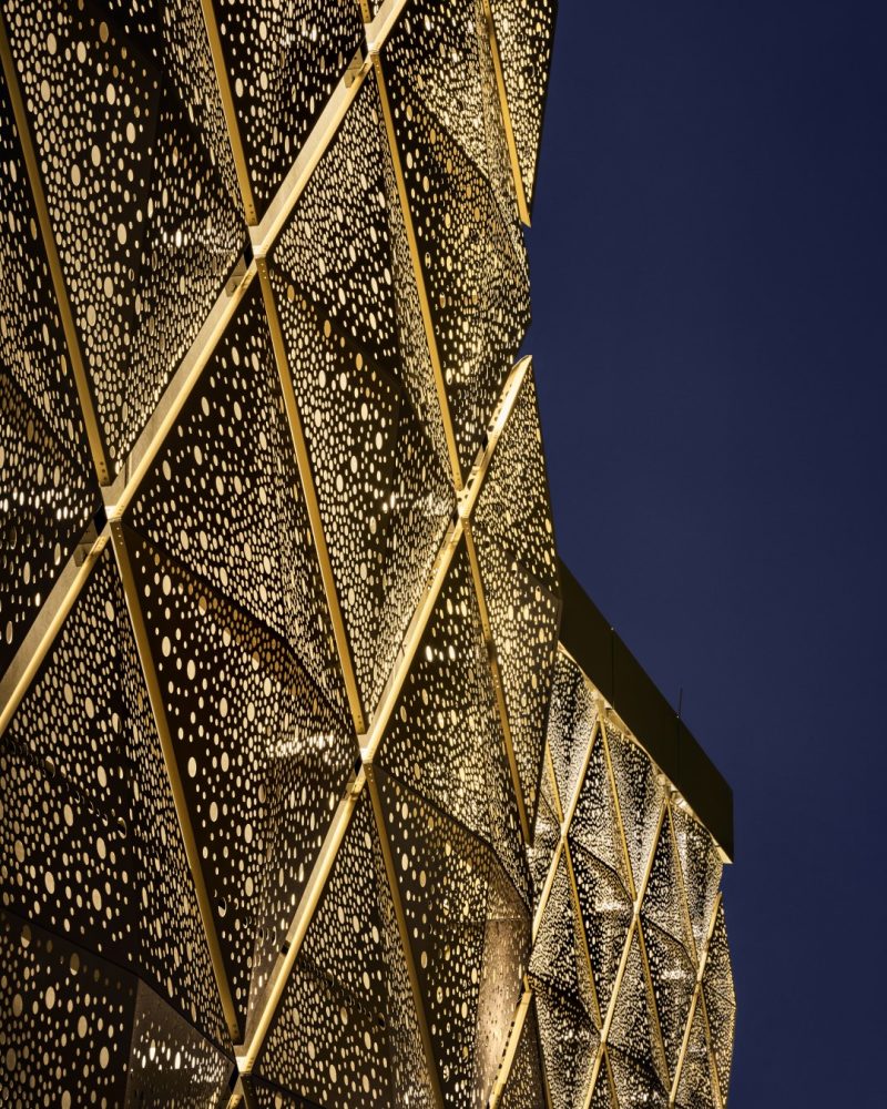 Close up of a facade of metal elements in gold with a dark blue sky in the background.