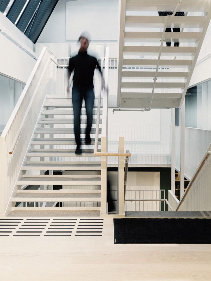Man in black walking down stairs in white inside an office.