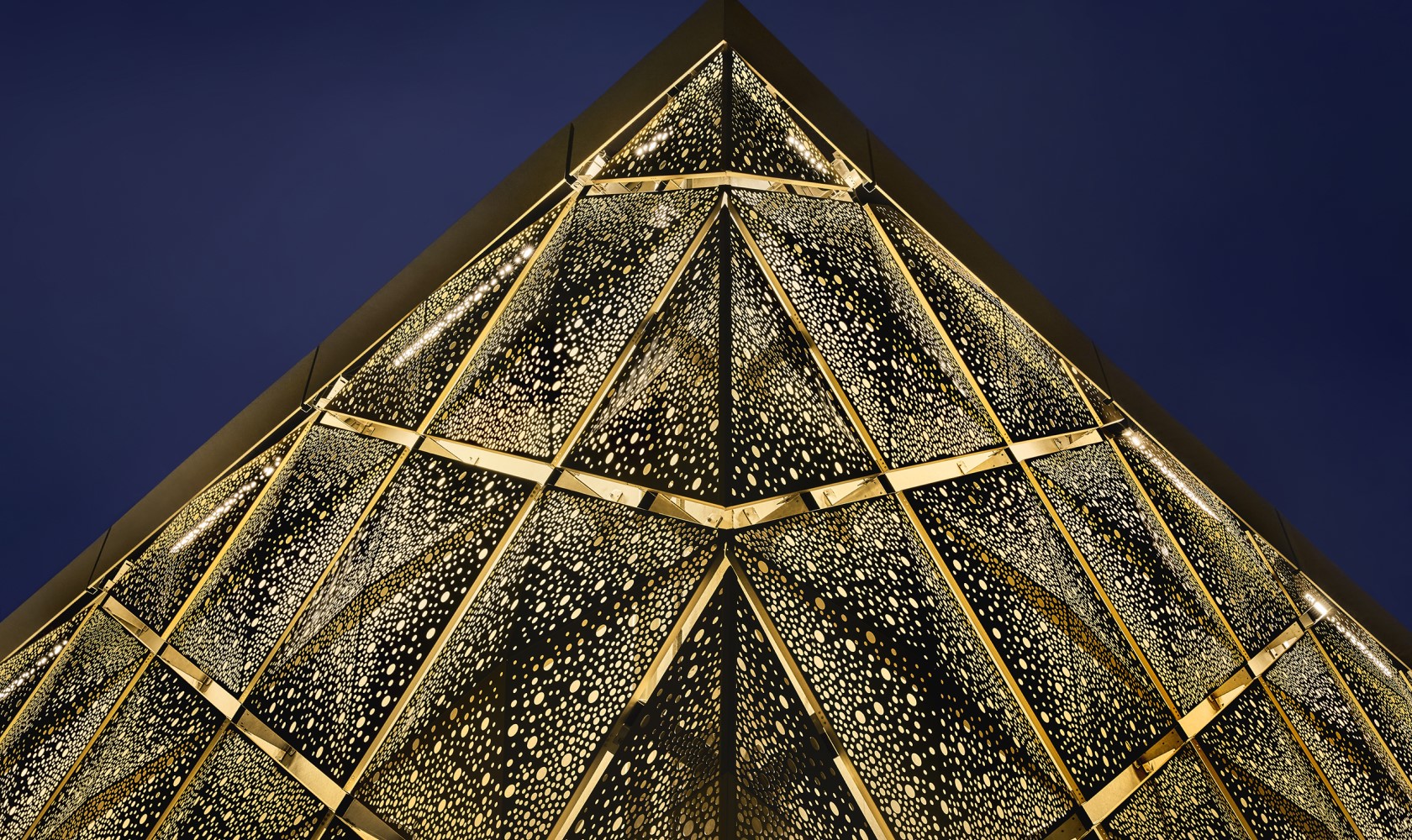 Close up of the corner of a building with an illuminated facade and a dark blue sky in the background.