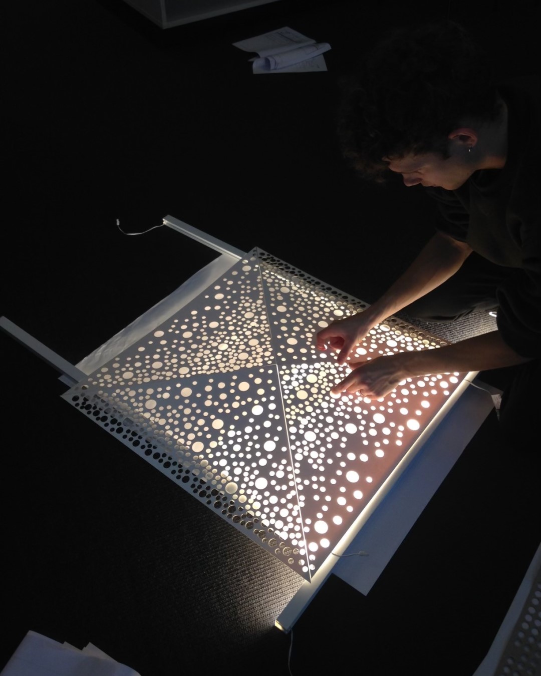 Hands working on a metal element in gold with a pattern of holes.