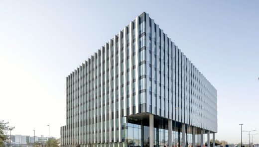 Corner view of office building, blue sky and a person on a bicycle on the road in front of the building.