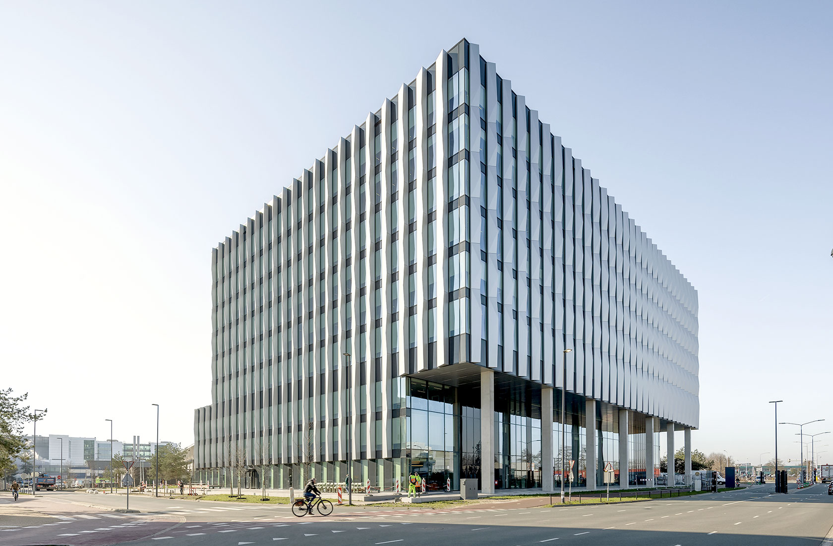 Corner view of office building, blue sky and a person on a bicycle on the road in front of the building.