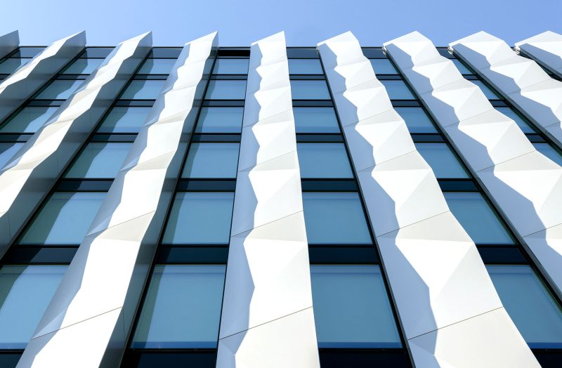 Close up of the facade of an office building with vertical white elements and windows.