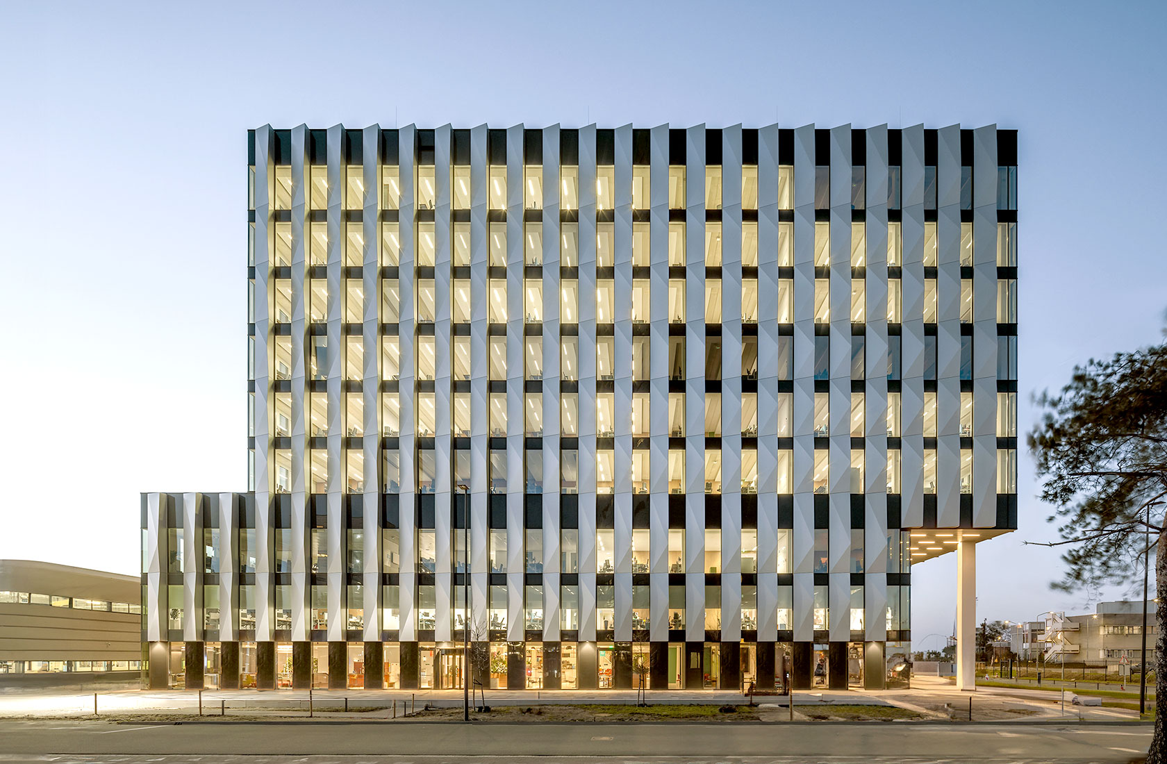 Nine storey officebuilding with blue sky in the background and a tree to the right.