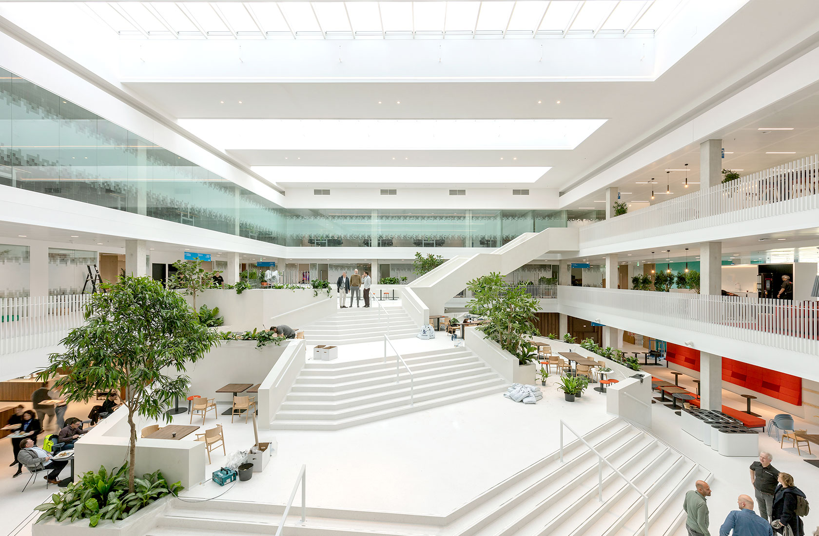 A plaza inside an office building with stairs in white and a green tree to the left.