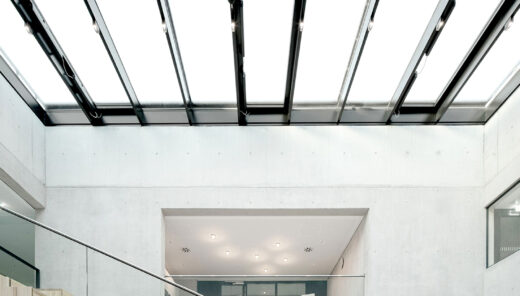 A larger open area where the walls are made of concrete and the lantern is made of glass. An open staircase solution with an oak staircase and glass railings.