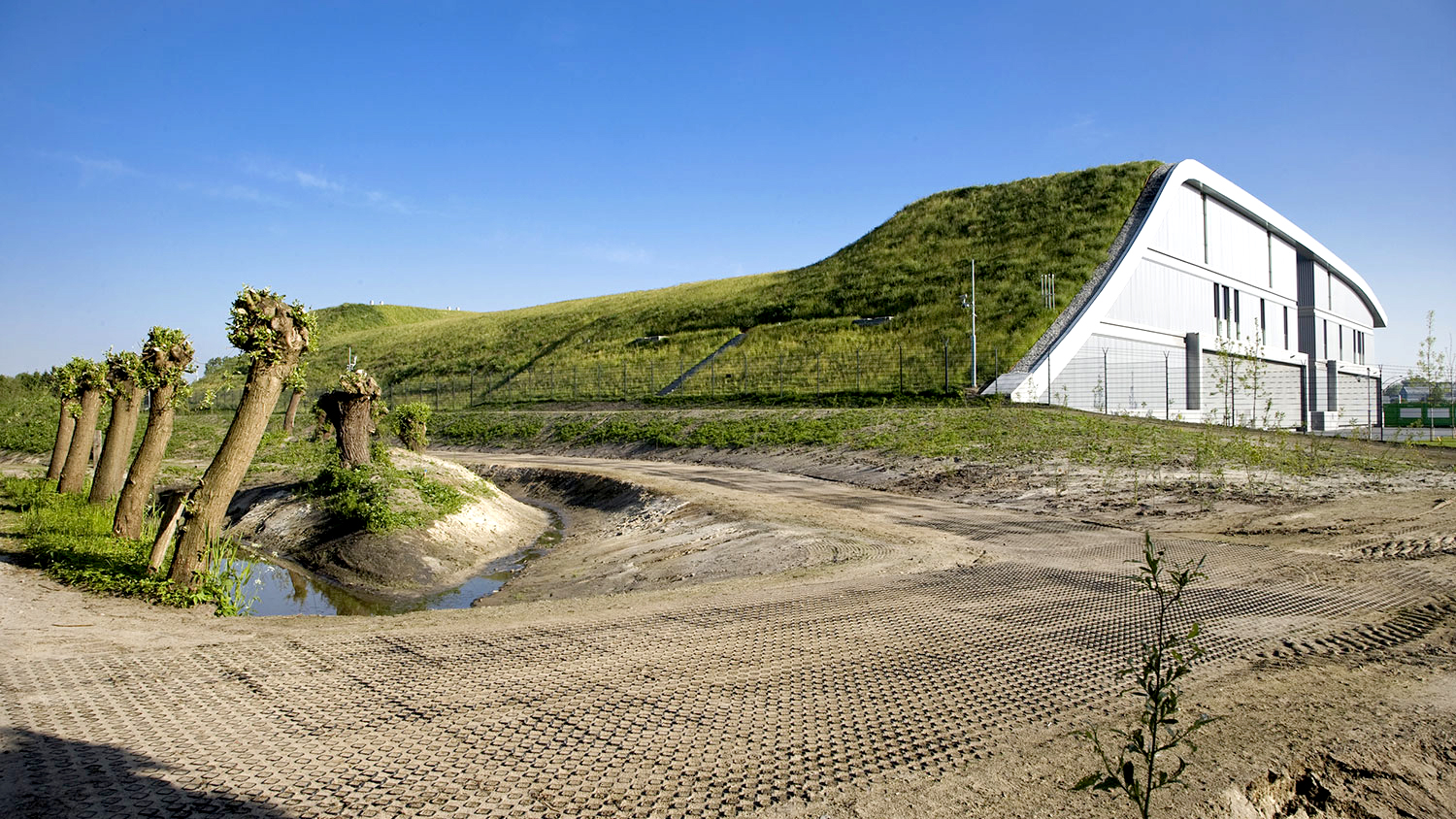 View from the back of the data center where the green roof creates a slope down to the ground. The side of the facade is in white and gray.