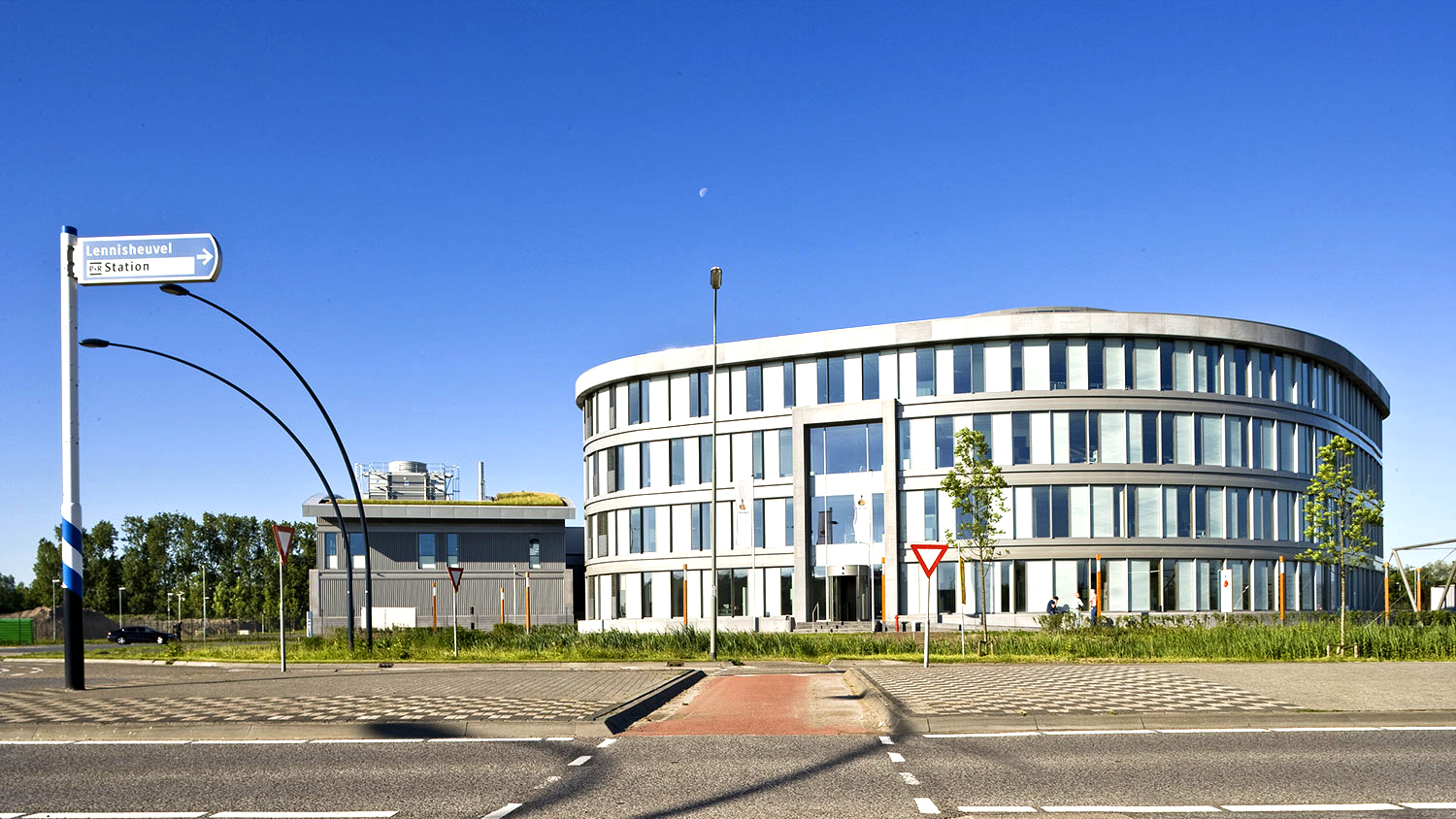 Four-story office building in white with large glass surfaces. There is a road in front of the building.