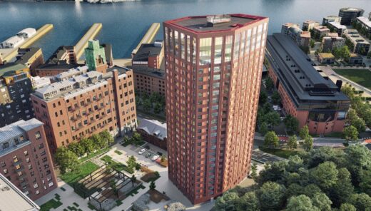 View from above on the 26-story high-rise residential building in red brick. Nice courtyard area to the left with stone paving, plantings, and trellises. To the right, a road and adjacent residential buildings.