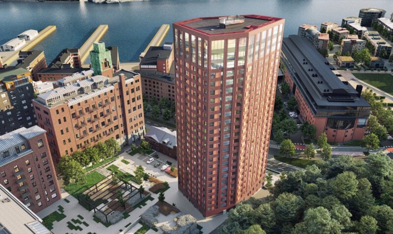 View from above on the 26-story high-rise residential building in red brick. Nice courtyard area to the left with stone paving, plantings, and trellises. To the right, a road and adjacent residential buildings.