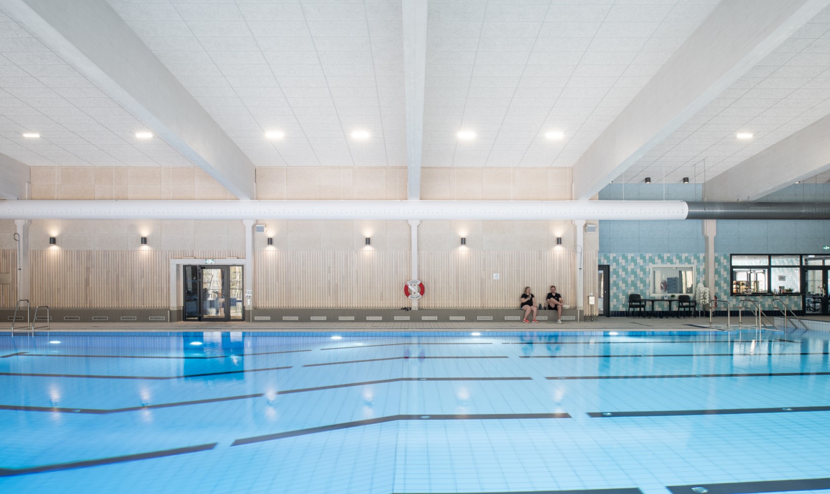 Interior image of a swimming pool from the long side where the pool gets deeper to the left. The far wall is covered in lighter wood.