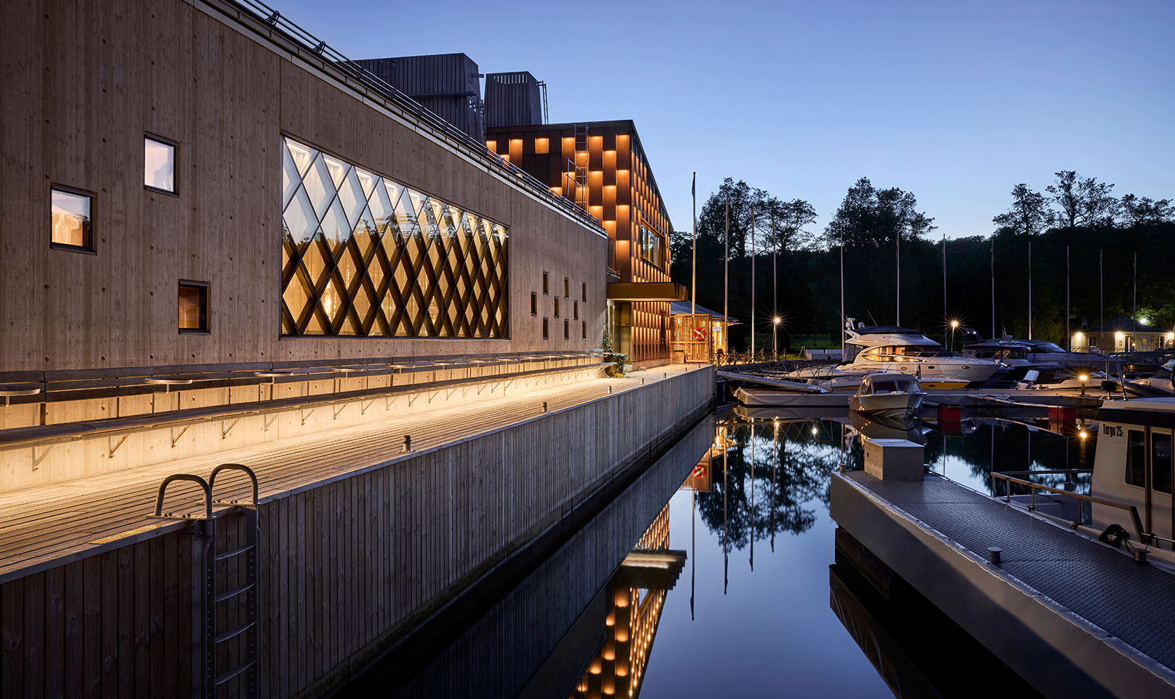 Backside of a restaurant building in wood with a larger glass section. The building is located right at the quayside.