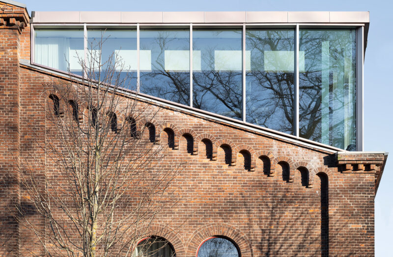 Close-up of the short side of an older brick building in red with an upper level entirely in glass.