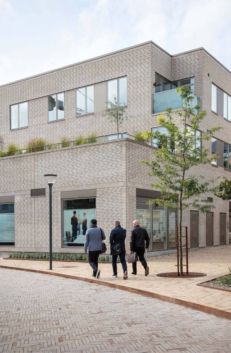 Three men are walking on a sidewalk in front of a new three-story house made of gray brick.