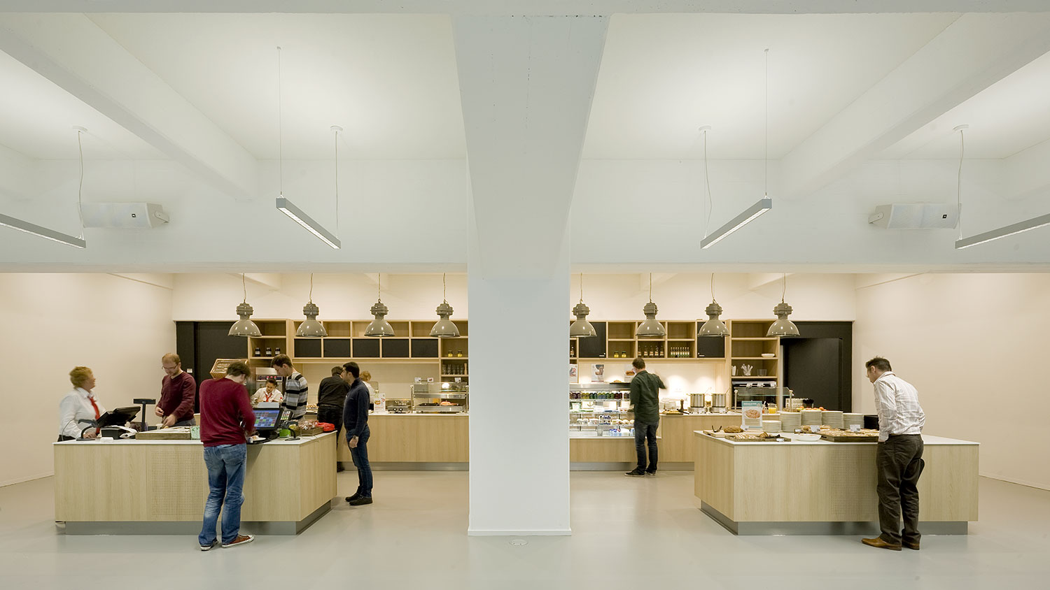 People serving themselves at buffet tables in light wood in a room with high ceilings.