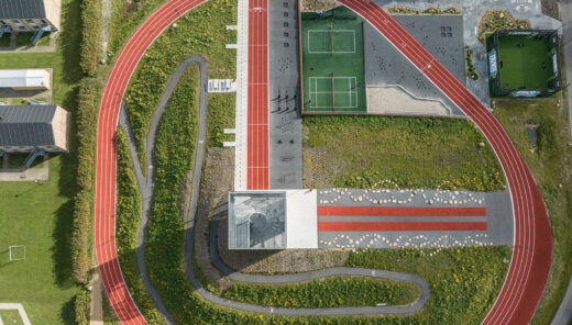 View from above of a sports facility on a green hill with red running tracks, playing fields, buildings, and other activity-based equipment.