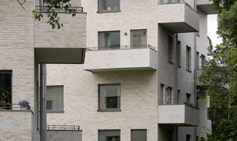 Close-up of a multi-storey building in beige brick, with the balconies extending from the building also made of brick.