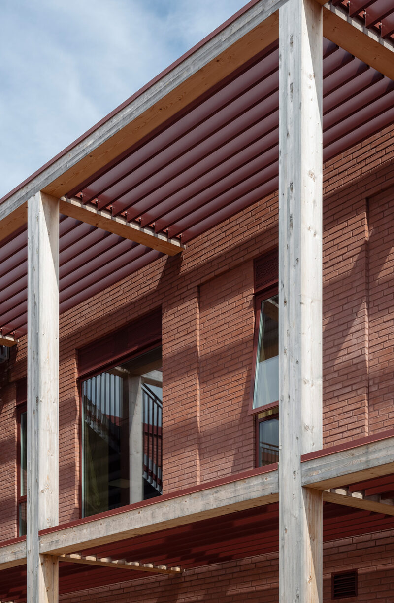 Close-up of the façade of a red brick building with exposed wooden beams set slightly away from the façade.