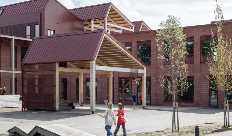Entrance to a school in red brick with two girls walking in the foreground.