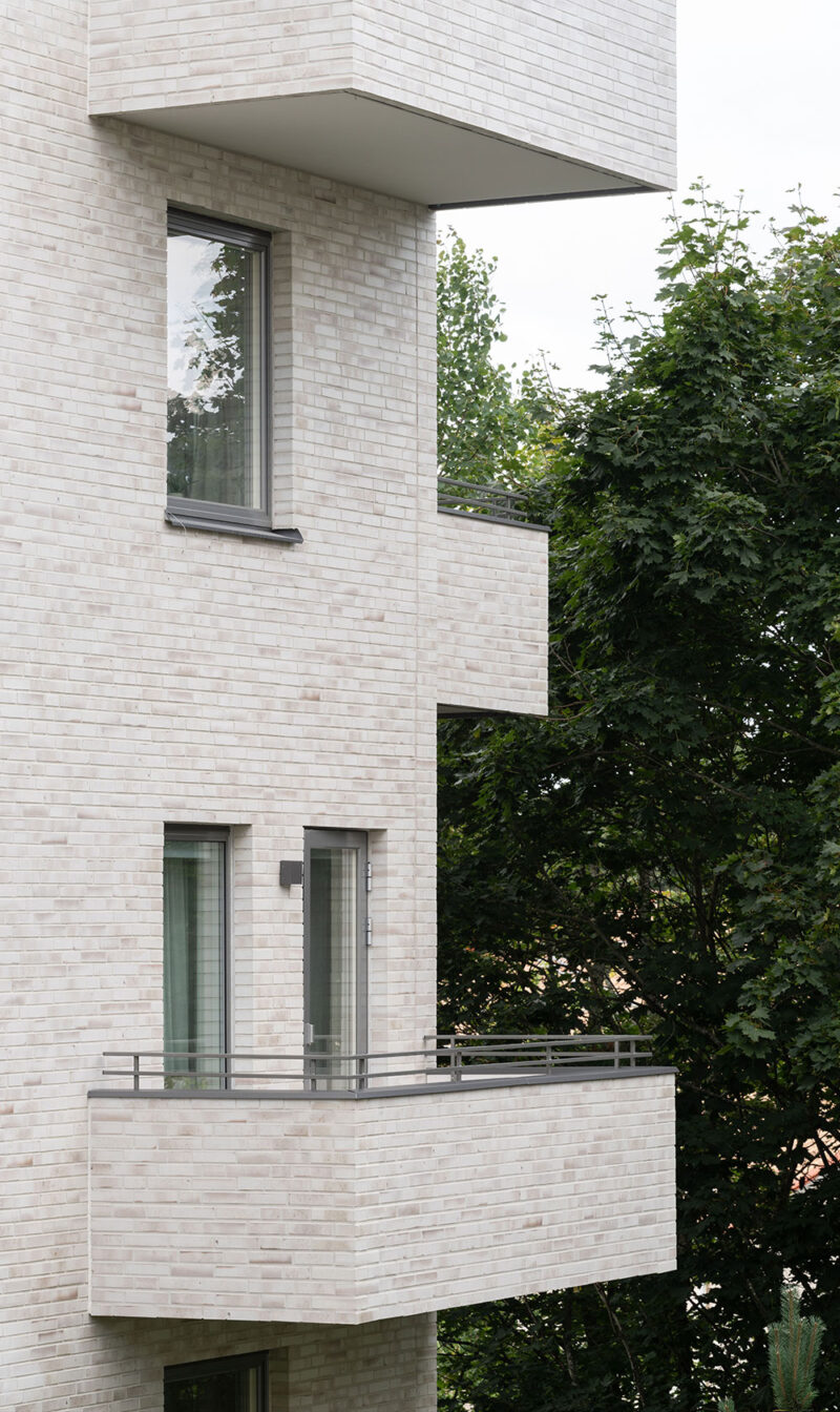 Close-up of the façade of a multi-storey building in brick, with a large tree to the right.