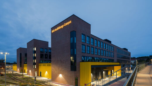 Three red brick buildings are placed parallel to each other, with lower yellow buildings between them that connect the buildings to one another. A railway yard to the left of the building.