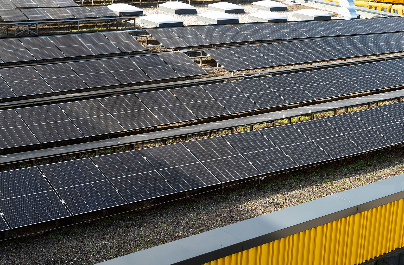 Several rows of solar panels on a roof, a yellow facade is glimpsed in the foreground.