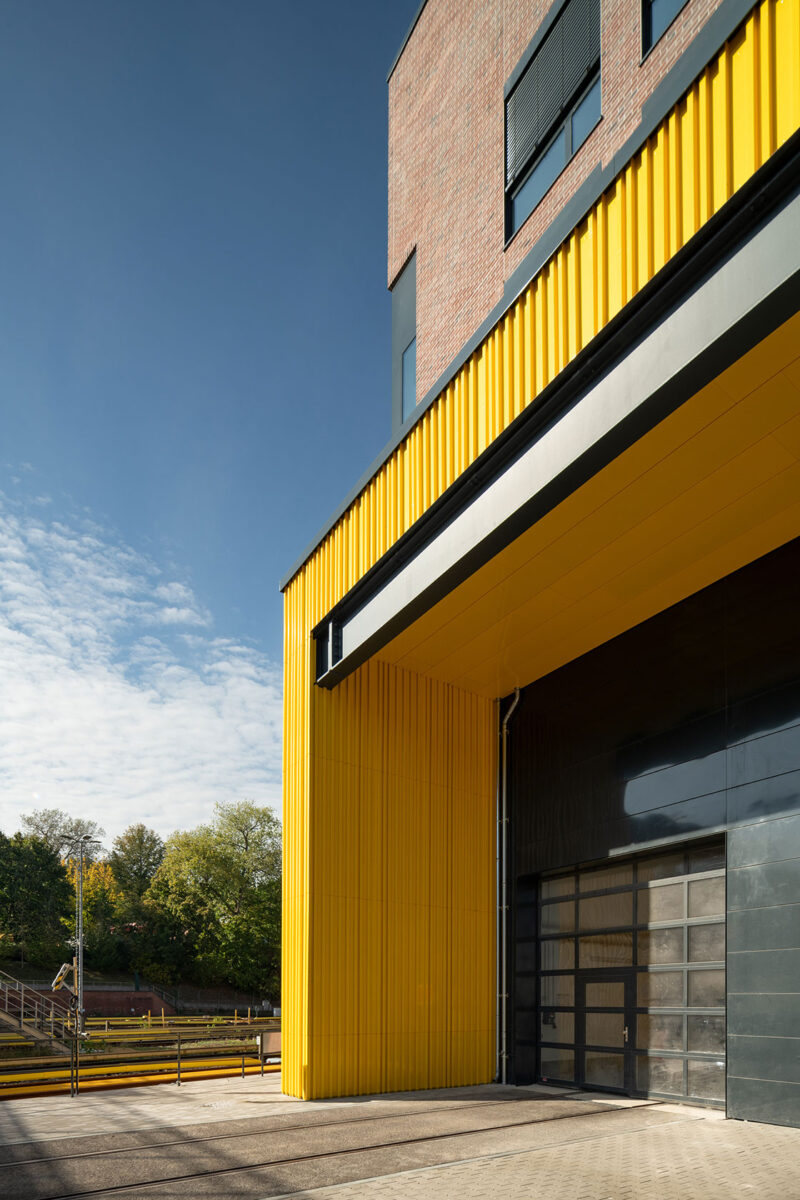 Close-up of the facade in red brick, window areas, and a lower protruding part in yellow.