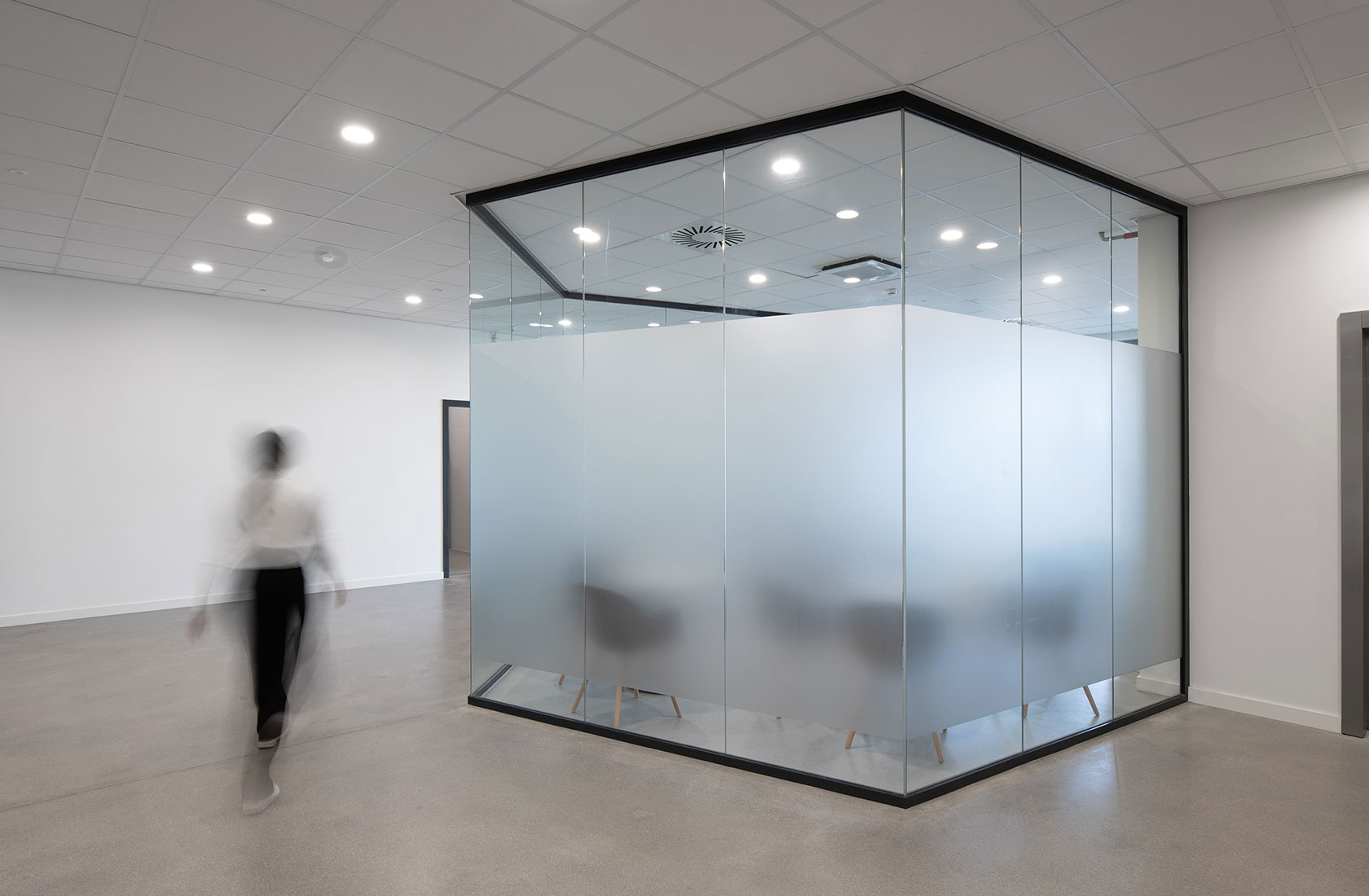A person passing by in a corridor outside a glazed conference room with frosted glass.