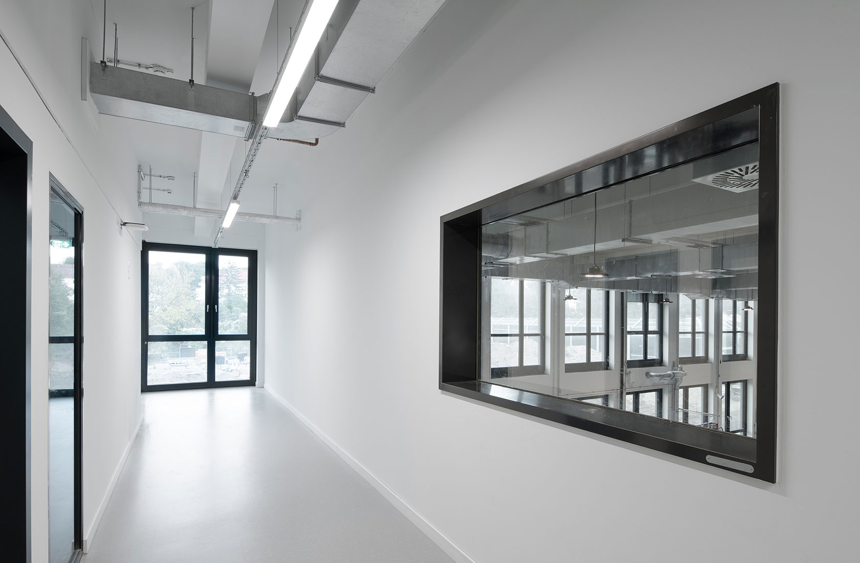 Corridor with white walls and light flooring, windows towards the workshop and outside.
