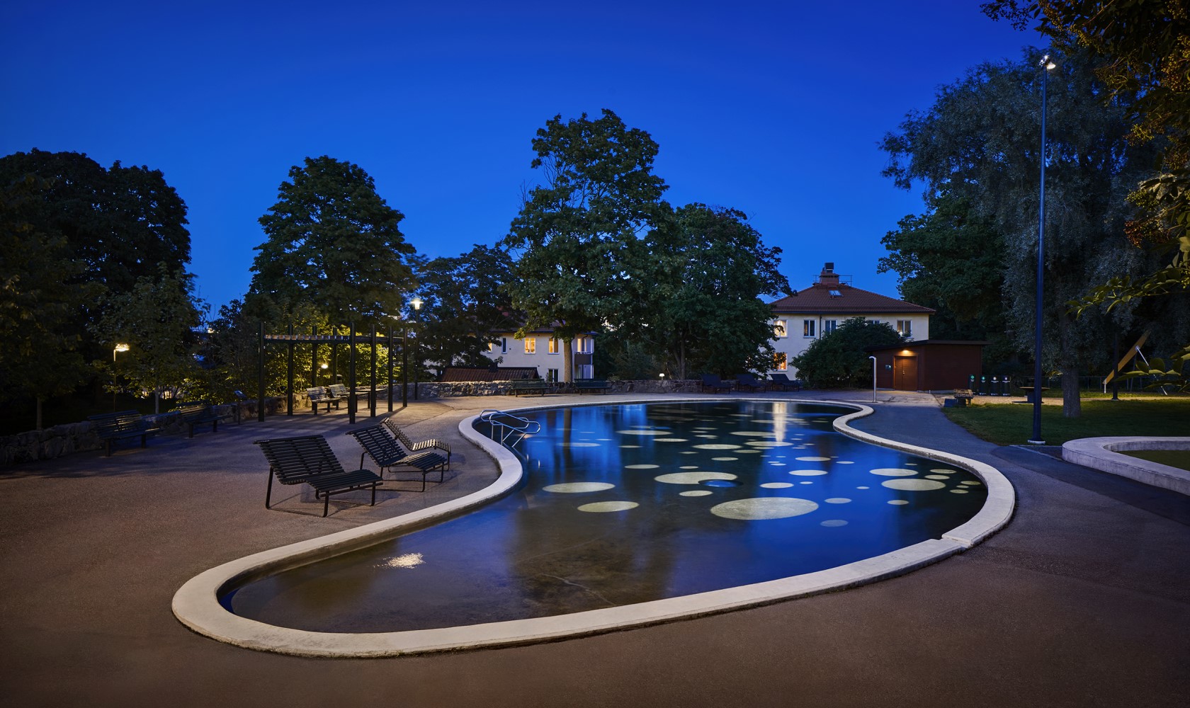 Organically shaped pond with lighting by the playground in a residential area.