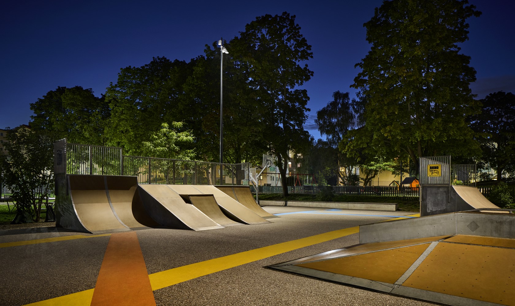 Evening picture of a skatepark with a green area in the background.
