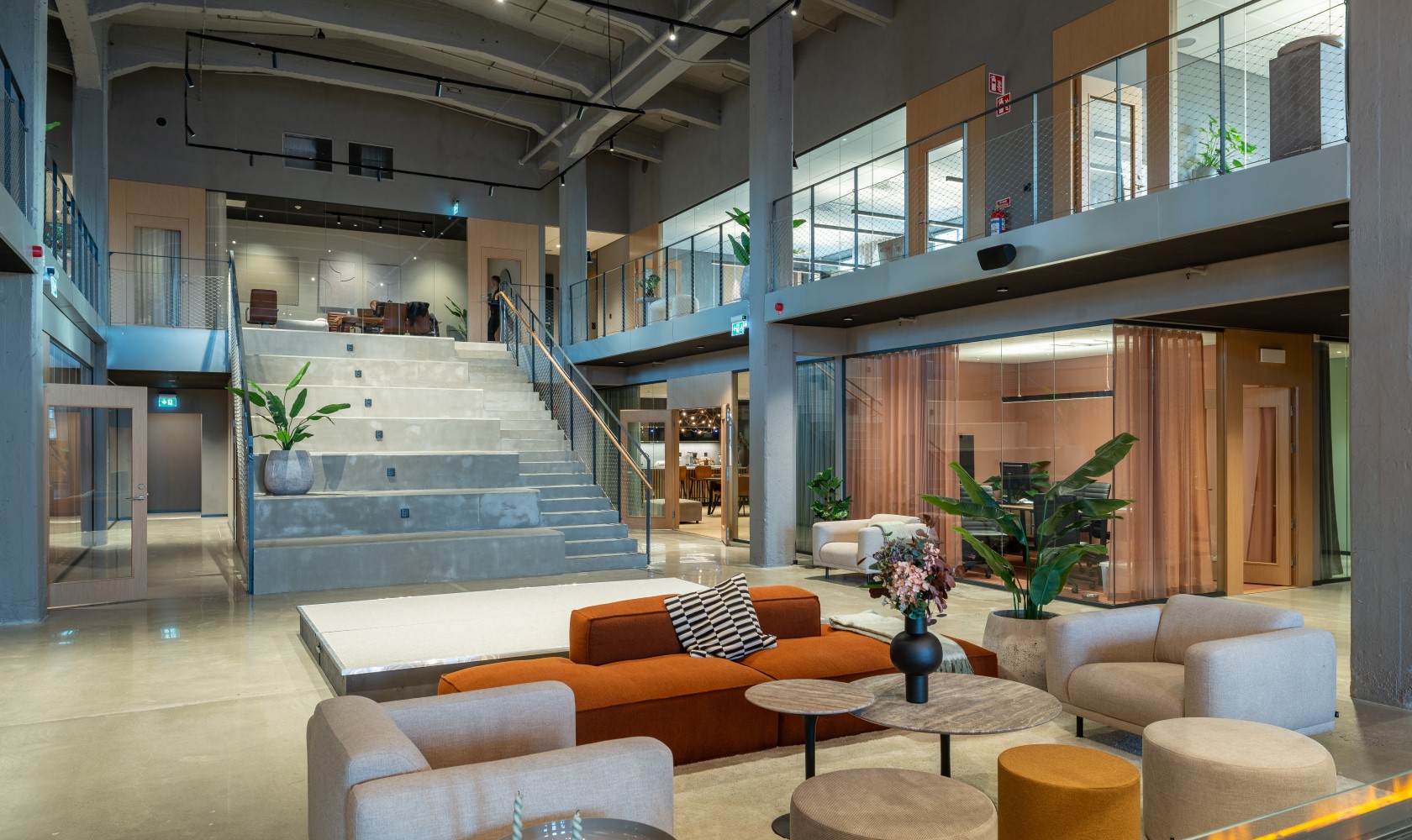 Open area in a larger office space with modern seating furniture in the foreground and a concrete staircase leading to the upper floor in the background.