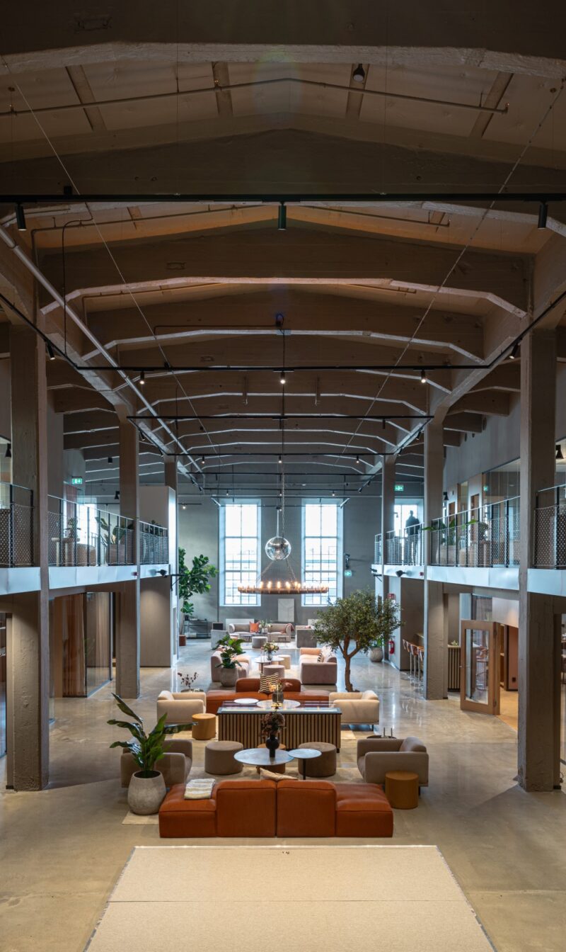 Lounge area with high ceilings in the centre and two floors on the sides in a converted industrial space.