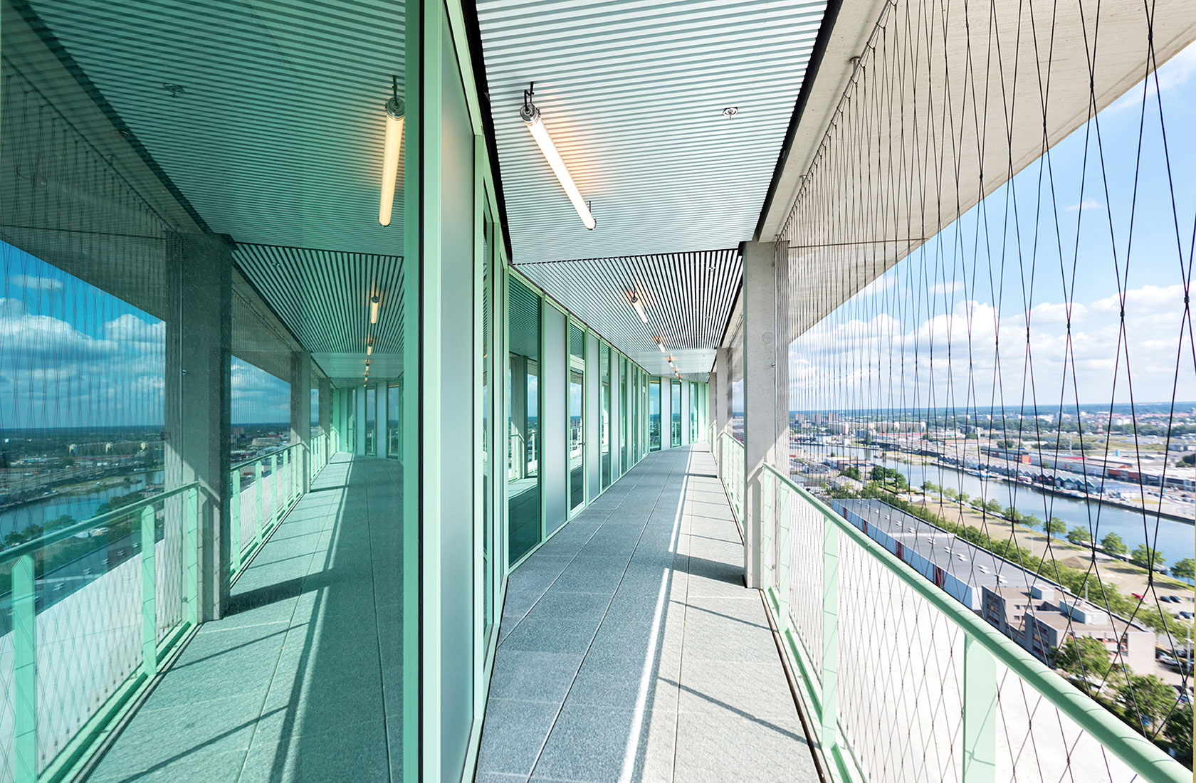 Outdoor passage along a tall building with a green facade and a view of the city.