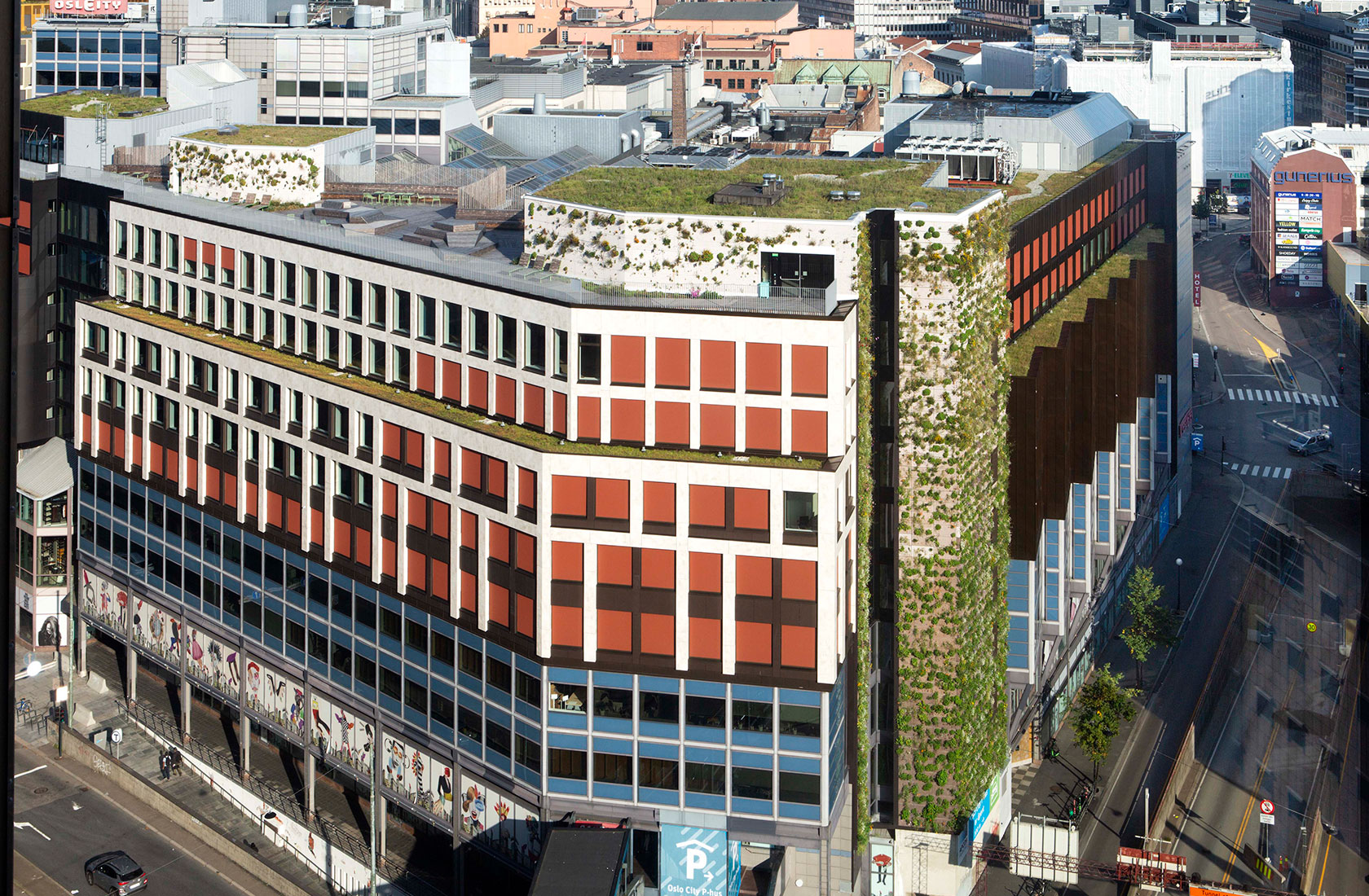 Image from above of a larger building in central Oslo that partially has a green facade and a large rooftop terrace with many green features.