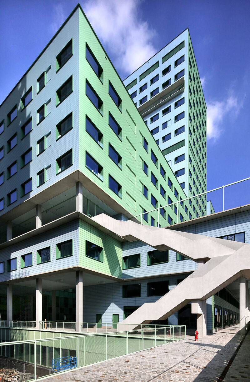 Green hospital building from a corner with an organically shaped gray staircase on the side.