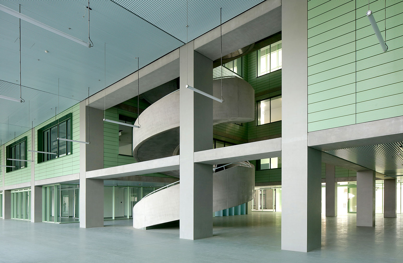 Part of the hospital corridor with a wider spiral staircase in gray leading to an upper level in the background.