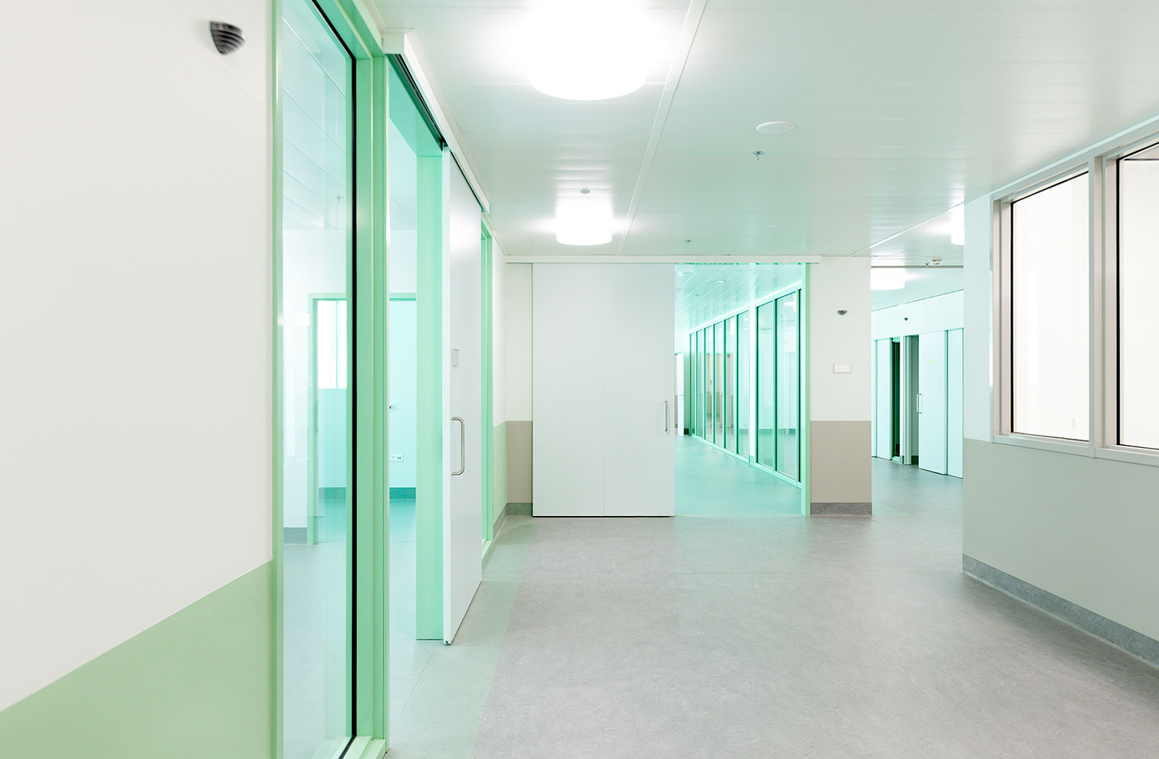 Empty hospital corridor with light walls and green sliding doors.