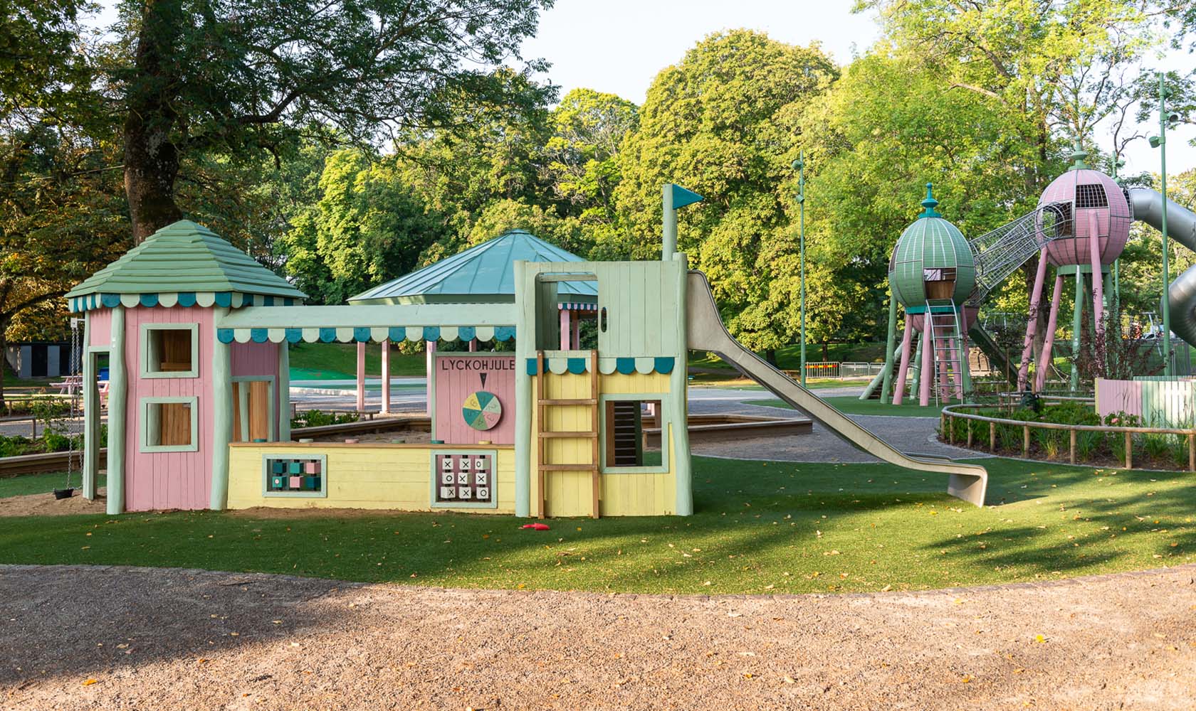 Tivoli-inspired playhouse and slides in a green park area.