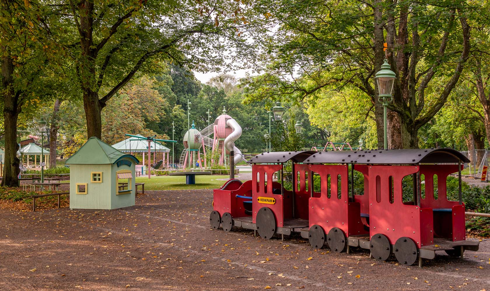 Playground area in a green park with a red train in the foreground
